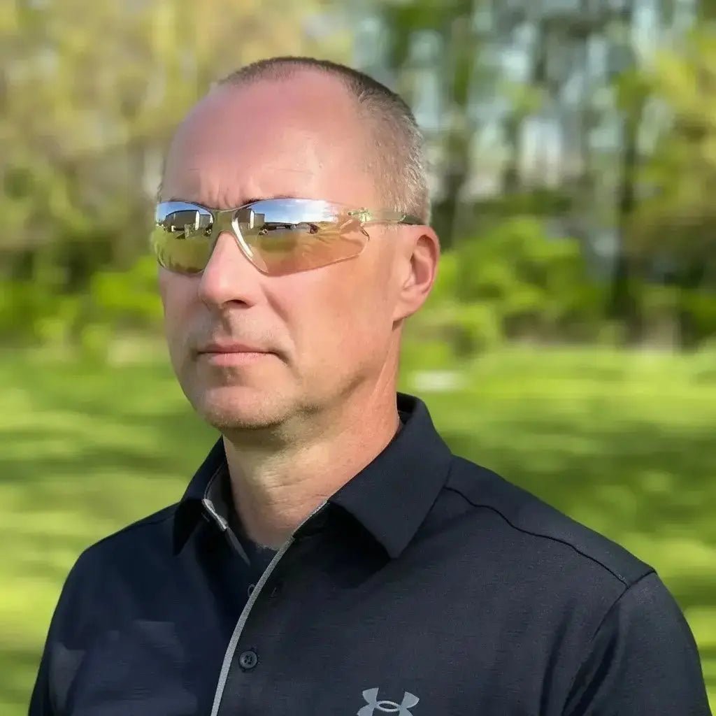 Man wearing clear tinted safety glasses outdoors with green grass and trees in the background